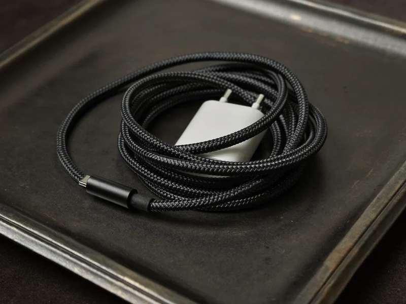 Pletený kabel USB-C stočený vedle malé bílé nabíječky na kovové tácu